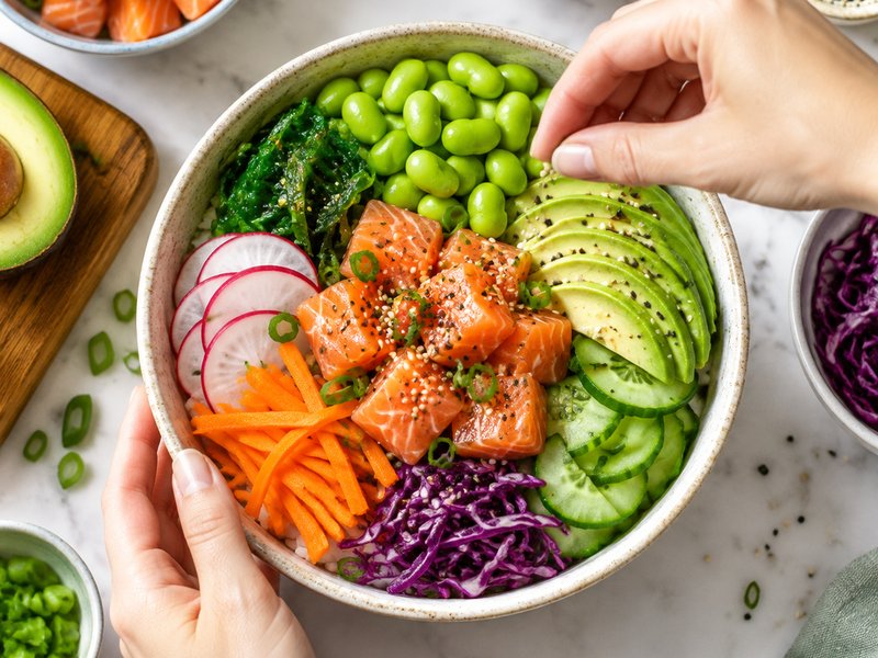 Hands finishing a colourful poke bowl, seen from above